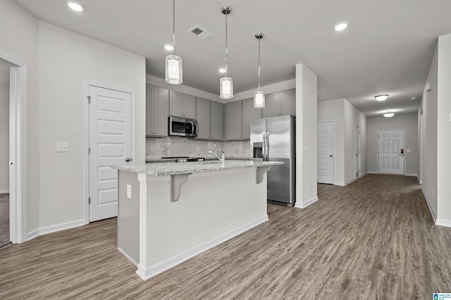 kitchen featuring hardwood / wood-style floors, light stone counters, stainless steel appliances, and an island with sink