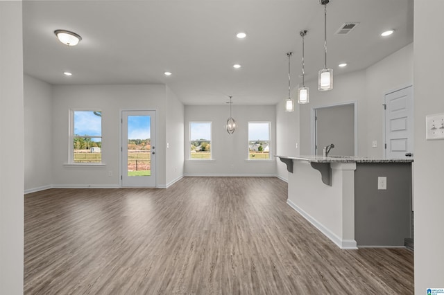 kitchen featuring sink, dark hardwood / wood-style floors, light stone countertops, decorative light fixtures, and a kitchen bar