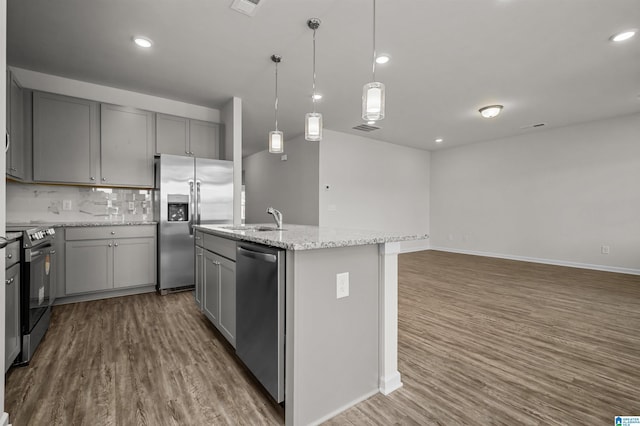 kitchen with light stone countertops, dark hardwood / wood-style flooring, stainless steel appliances, sink, and an island with sink