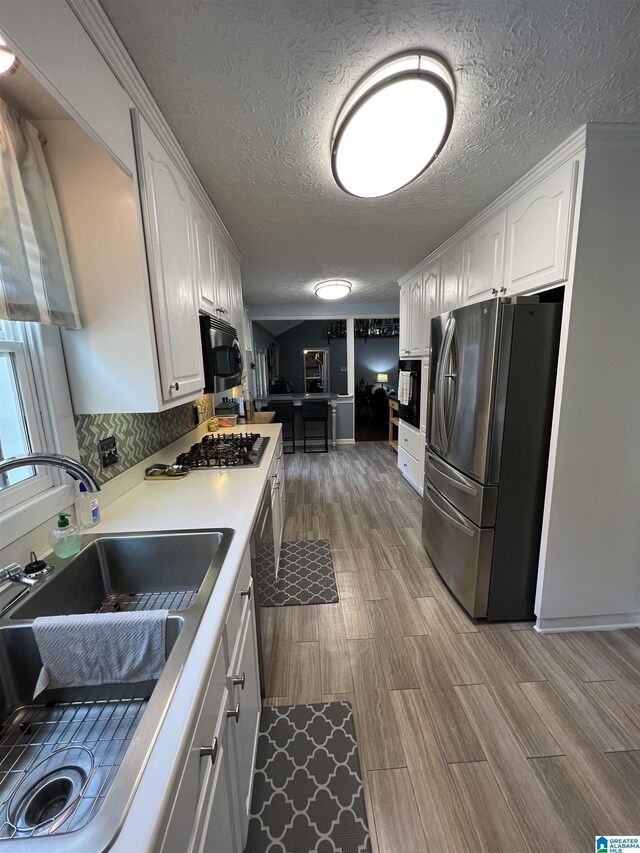 kitchen with a textured ceiling, light hardwood / wood-style flooring, stainless steel appliances, sink, and white cabinets