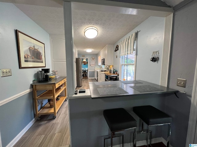 kitchen featuring white cabinets, light hardwood / wood-style flooring, stainless steel refrigerator, kitchen peninsula, and a textured ceiling