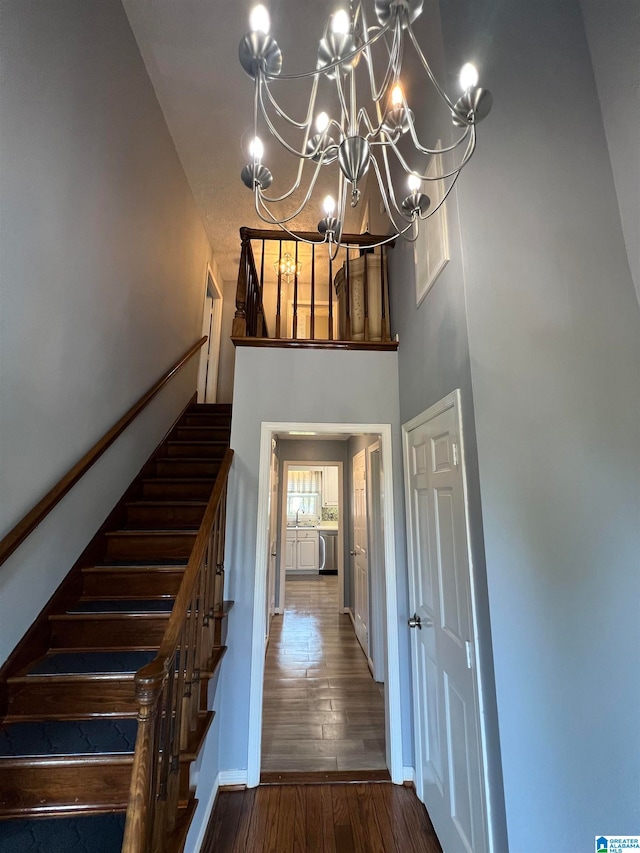 stairs with a high ceiling, a notable chandelier, and wood-type flooring