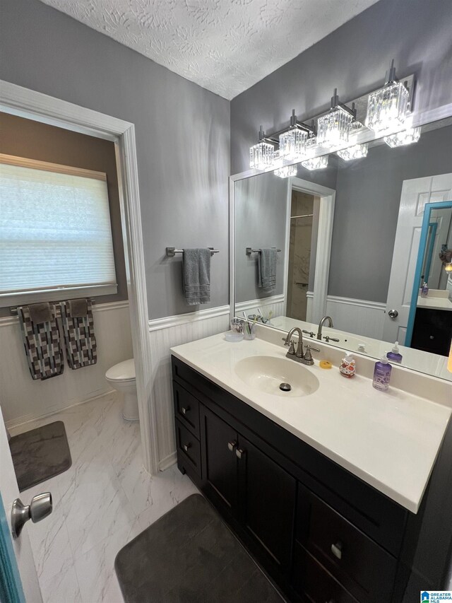 bathroom with a textured ceiling, vanity, toilet, and wooden walls