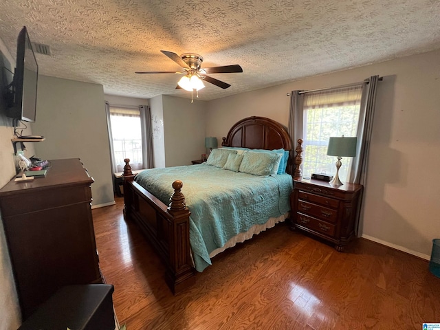 bedroom with a textured ceiling, dark wood-type flooring, ceiling fan, and multiple windows