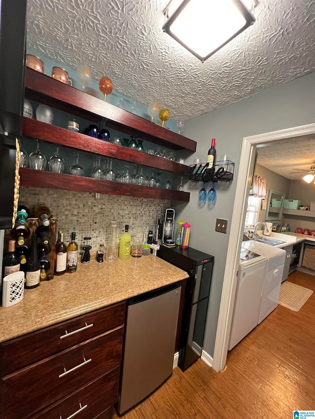 bar featuring separate washer and dryer, light hardwood / wood-style flooring, dishwasher, and decorative backsplash