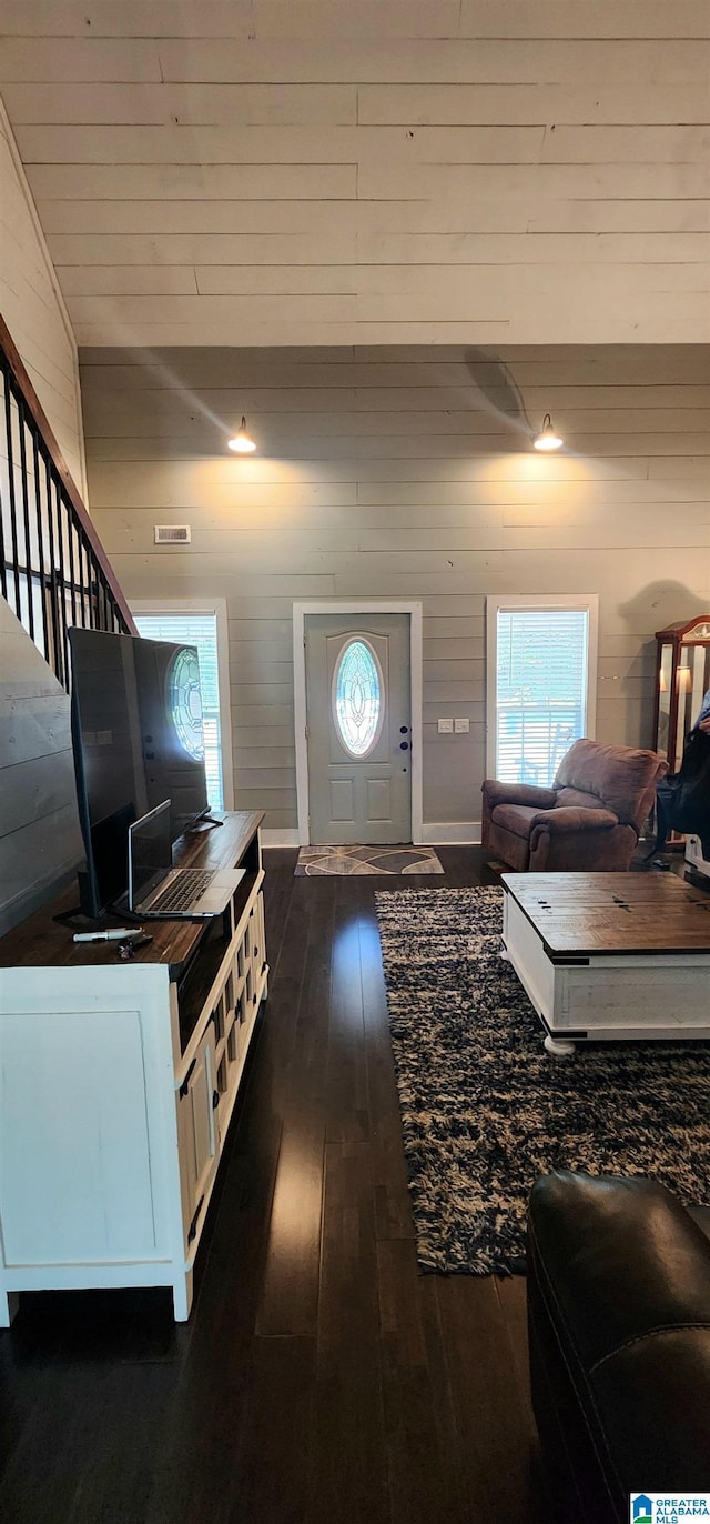 living area with wood walls, lofted ceiling, visible vents, and dark wood finished floors