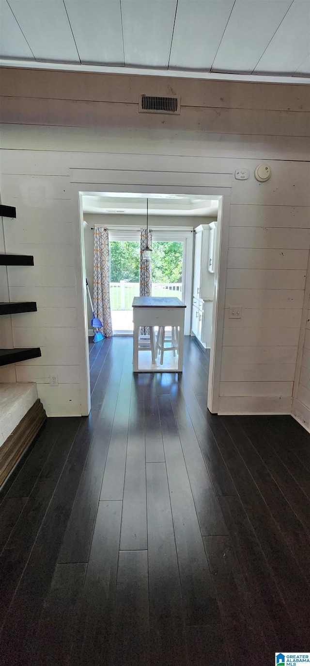 living area featuring wood walls, vaulted ceiling, dark wood-style floors, and visible vents