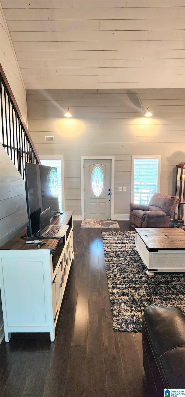 living area featuring wood walls, vaulted ceiling, dark wood-style floors, and visible vents