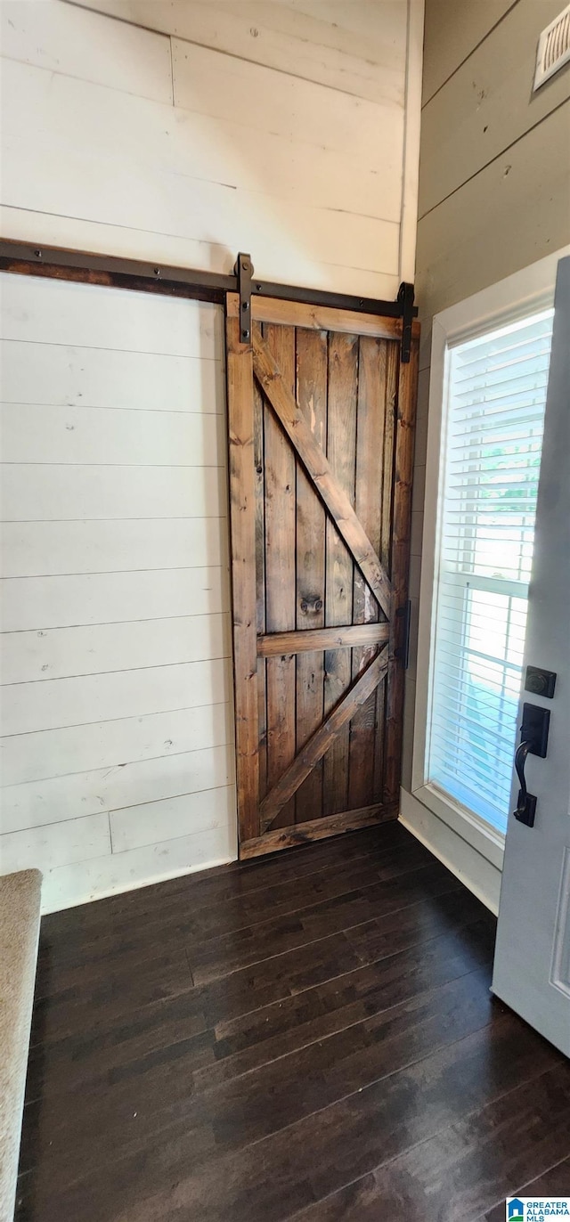 interior space with wood finished floors, wooden walls, visible vents, and a barn door