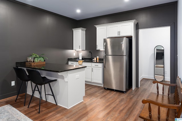 kitchen featuring a breakfast bar, stainless steel refrigerator, sink, hardwood / wood-style flooring, and white cabinetry