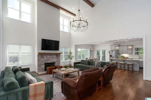 living room with a chandelier, wood-type flooring, a stone fireplace, beam ceiling, and a towering ceiling