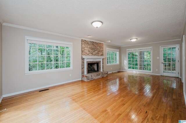 unfurnished living room with a fireplace, a textured ceiling, a wealth of natural light, and light hardwood / wood-style floors