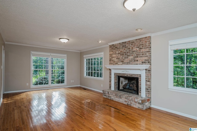 unfurnished living room featuring light hardwood / wood-style flooring, ornamental molding, a textured ceiling, and a brick fireplace