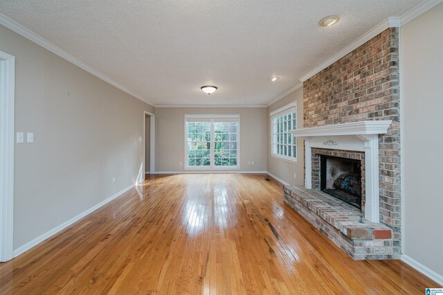 unfurnished living room featuring light hardwood / wood-style flooring, crown molding, a textured ceiling, and a brick fireplace