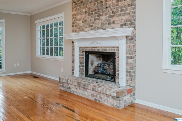 unfurnished living room with light wood-type flooring, plenty of natural light, crown molding, and a brick fireplace