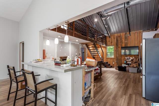 kitchen featuring wood walls, stainless steel fridge, decorative light fixtures, dark wood-type flooring, and high vaulted ceiling