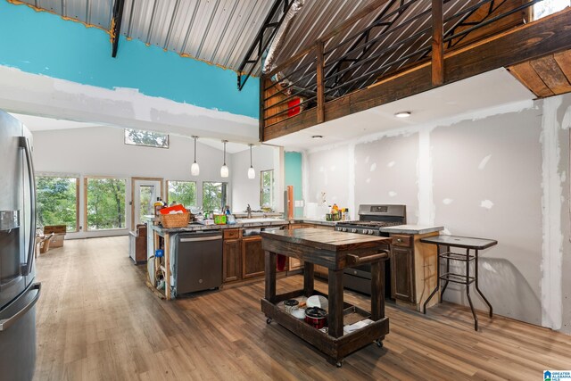 kitchen with high vaulted ceiling, decorative light fixtures, stainless steel appliances, a center island, and dark wood-type flooring