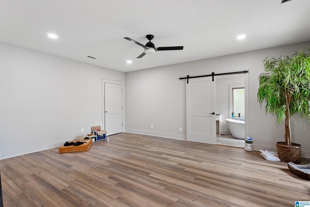 interior space featuring ensuite bath, hardwood / wood-style flooring, ceiling fan, and a barn door