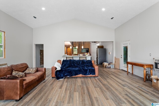 living room with high vaulted ceiling, plenty of natural light, heating unit, and wood-type flooring