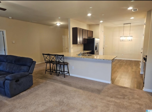 kitchen with light stone counters, hanging light fixtures, kitchen peninsula, stainless steel refrigerator with ice dispenser, and ceiling fan with notable chandelier