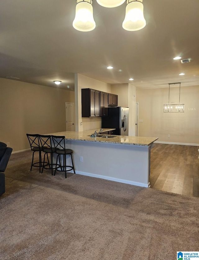 kitchen with stainless steel refrigerator with ice dispenser, kitchen peninsula, light stone counters, and decorative light fixtures