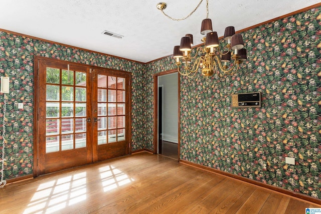 spare room with crown molding, french doors, hardwood / wood-style floors, a chandelier, and a textured ceiling