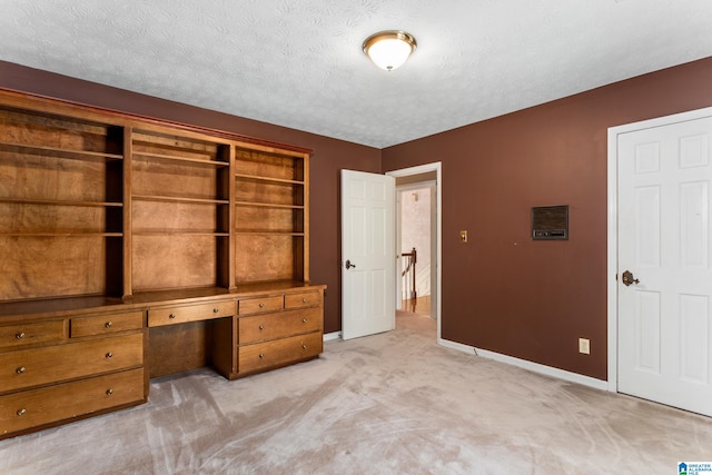 unfurnished bedroom featuring built in desk, light colored carpet, and a textured ceiling