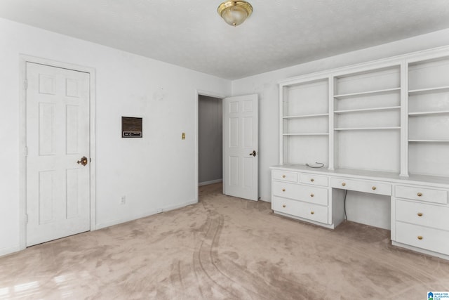 unfurnished bedroom with light carpet, built in desk, and a textured ceiling