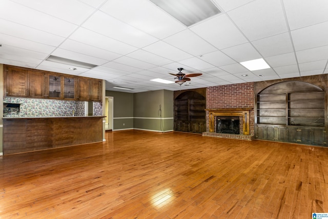 unfurnished living room with a fireplace, hardwood / wood-style floors, built in shelves, a drop ceiling, and ceiling fan