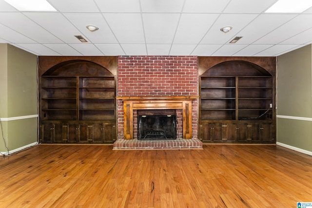 unfurnished living room with built in shelves, a paneled ceiling, hardwood / wood-style floors, and a fireplace