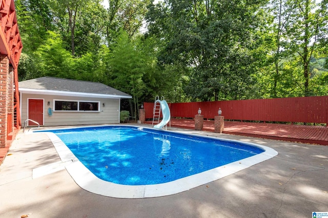 view of swimming pool with a water slide, an outbuilding, and a patio