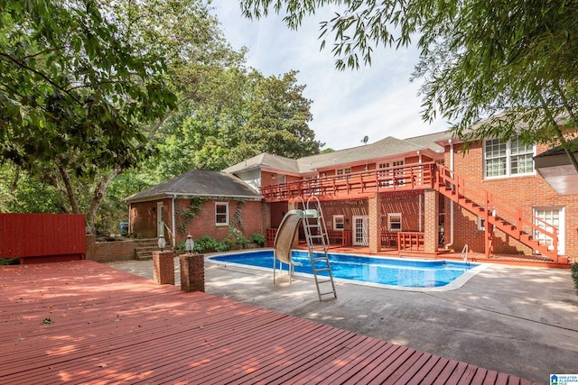 view of pool with a water slide, a patio area, and a wooden deck