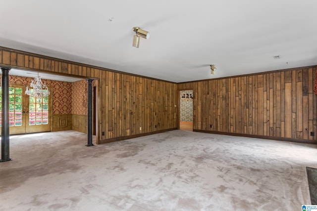 carpeted empty room with french doors, an inviting chandelier, and wooden walls