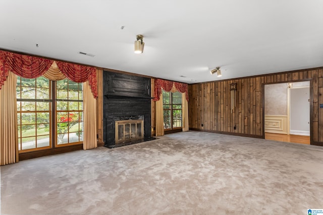 unfurnished living room featuring a wealth of natural light, carpet flooring, wood walls, and a fireplace