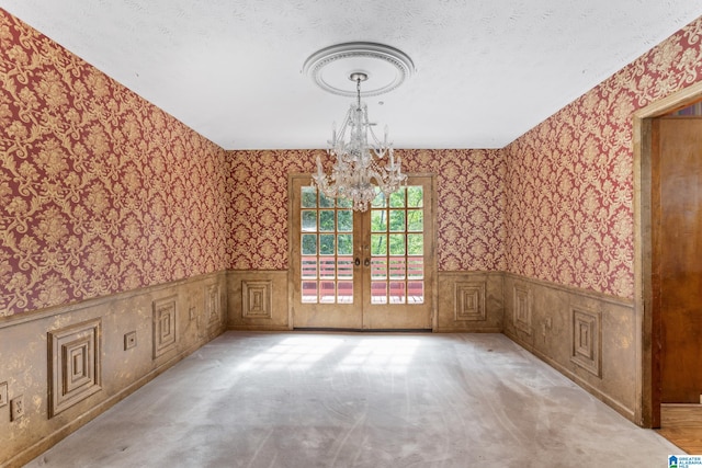 carpeted spare room with a notable chandelier, a textured ceiling, and french doors