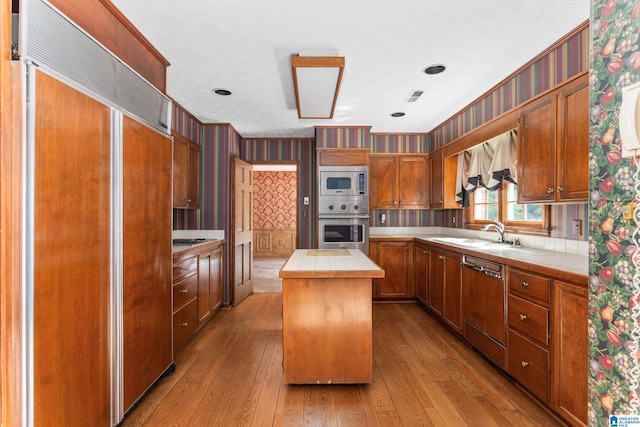 kitchen with built in appliances, tile countertops, light hardwood / wood-style flooring, a kitchen island, and sink