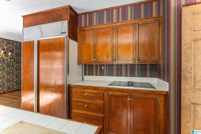 kitchen featuring a textured ceiling, paneled refrigerator, light hardwood / wood-style flooring, tile countertops, and stainless steel stovetop