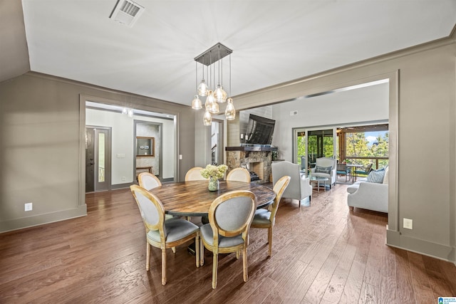 dining space with a notable chandelier, hardwood / wood-style flooring, vaulted ceiling, and a fireplace