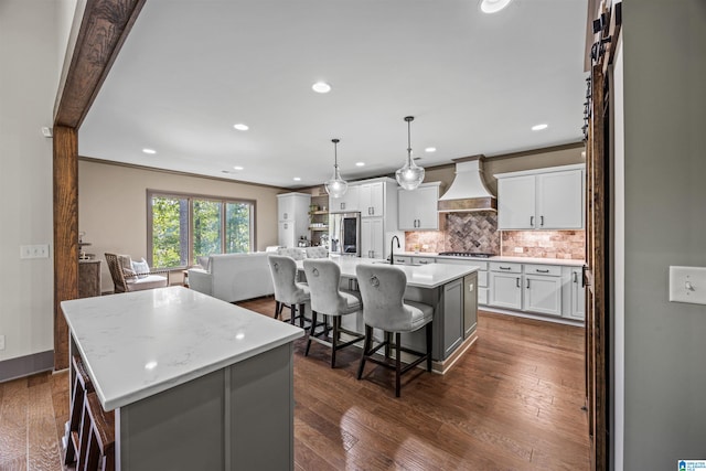 kitchen with dark hardwood / wood-style flooring, white cabinetry, pendant lighting, custom exhaust hood, and a center island with sink