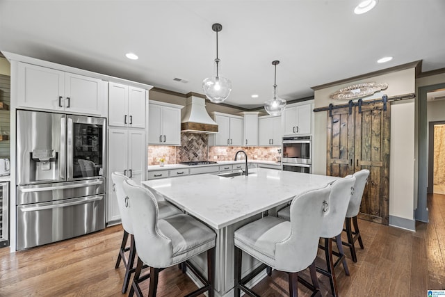 kitchen with hardwood / wood-style floors, hanging light fixtures, a barn door, custom range hood, and stainless steel appliances