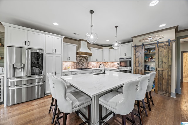 kitchen featuring hardwood / wood-style floors, premium range hood, a barn door, stainless steel appliances, and decorative light fixtures