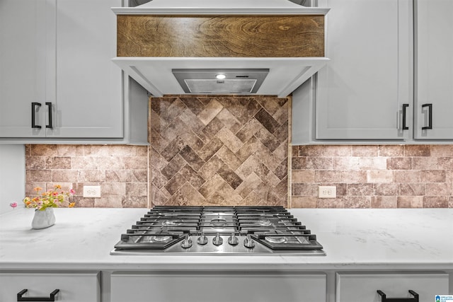 kitchen with stainless steel gas cooktop, custom exhaust hood, gray cabinetry, and backsplash