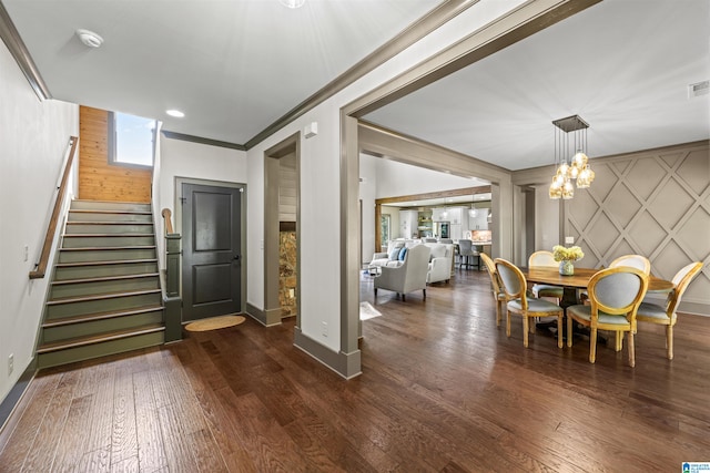 entrance foyer with dark wood-type flooring, ornamental molding, and a chandelier