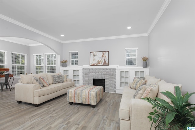 living room with crown molding, a brick fireplace, light hardwood / wood-style flooring, and a wealth of natural light