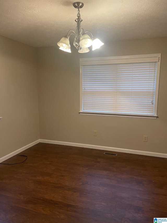 empty room with dark wood-type flooring, a textured ceiling, and a notable chandelier