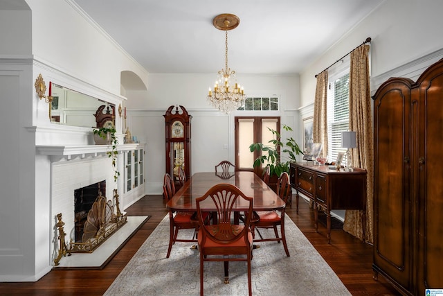 dining area featuring ornamental molding, dark wood-type flooring, an inviting chandelier, and a fireplace