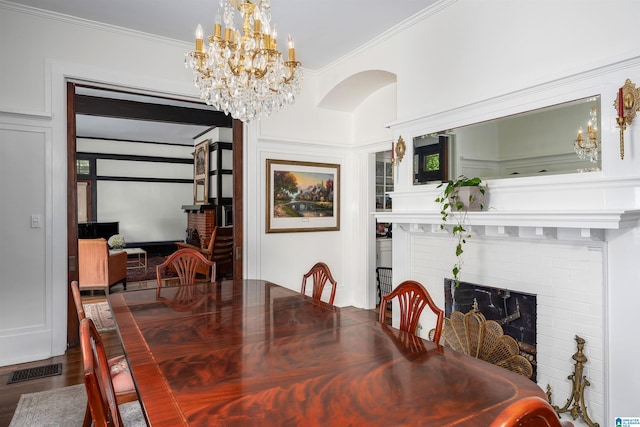 dining area featuring crown molding, wood finished floors, a chandelier, a brick fireplace, and visible vents
