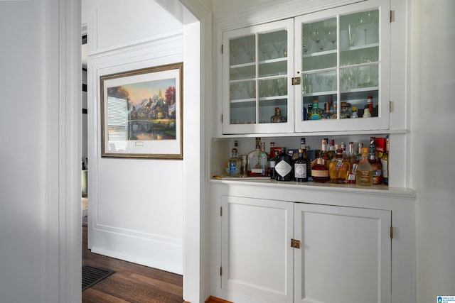 bar with dark hardwood / wood-style floors and white cabinets