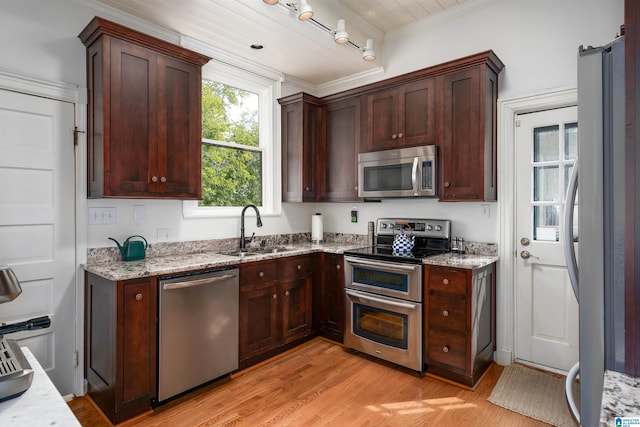 kitchen with light stone counters, a sink, light wood-type flooring, stainless steel appliances, and ornamental molding