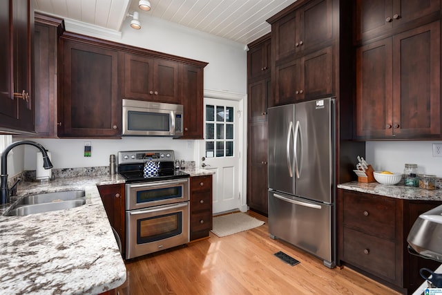 kitchen with light wood-type flooring, ornamental molding, sink, light stone countertops, and appliances with stainless steel finishes